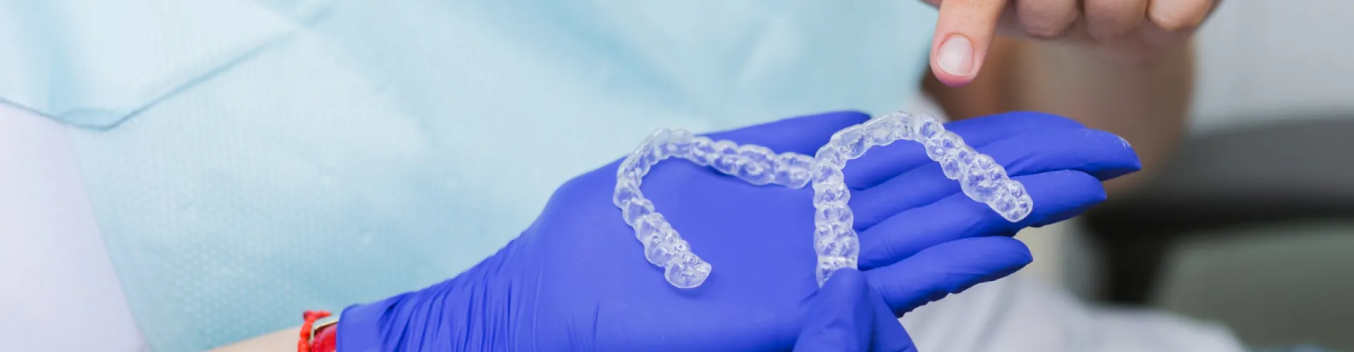 Gloved hand holding two clear aligners.