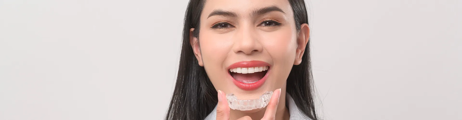Woman putting clear aligner in mouth.