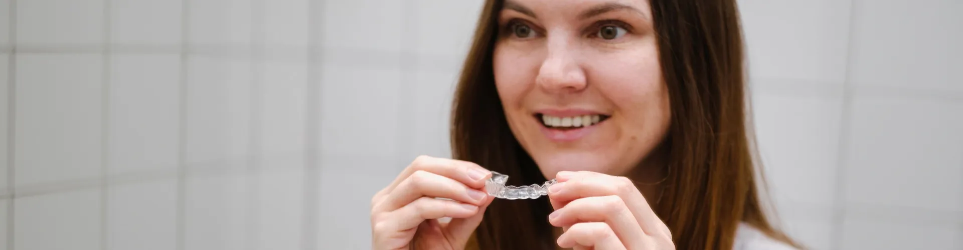Smiling woman holding clear aligner in front of her mouth.