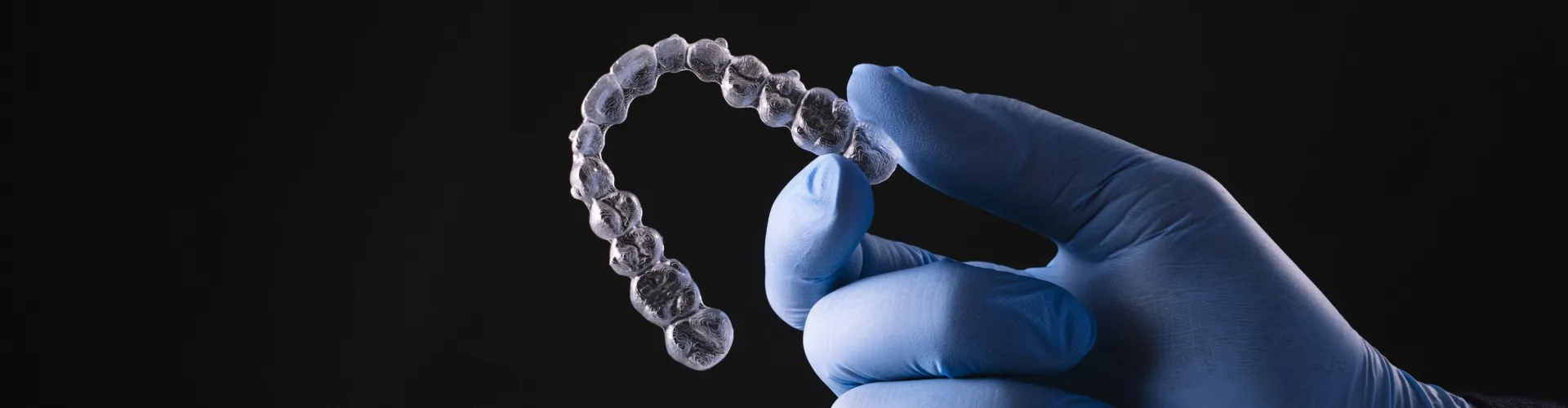 Gloved hand holding clear aligner.