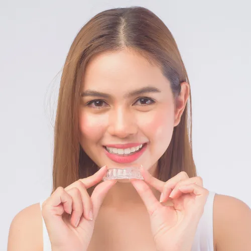 Smiling woman holding clear aligner in front of her mouth.