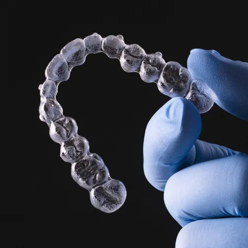Gloved hand holding clear aligner.