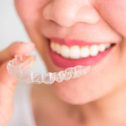 Woman holding clear aligner in front of mouth.