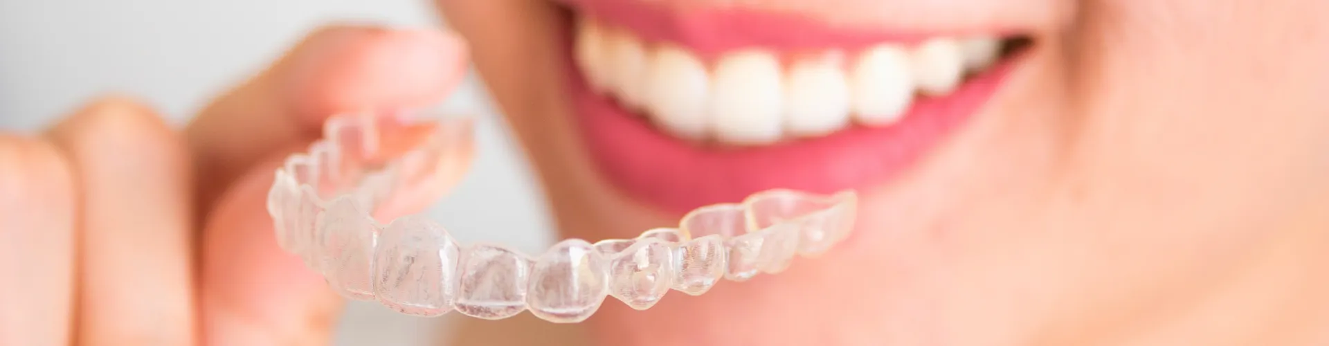 Woman holding clear aligner in front of mouth.
