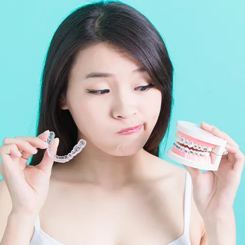 woman holding clear aligner in one hand and mouth model wearing braces in the other