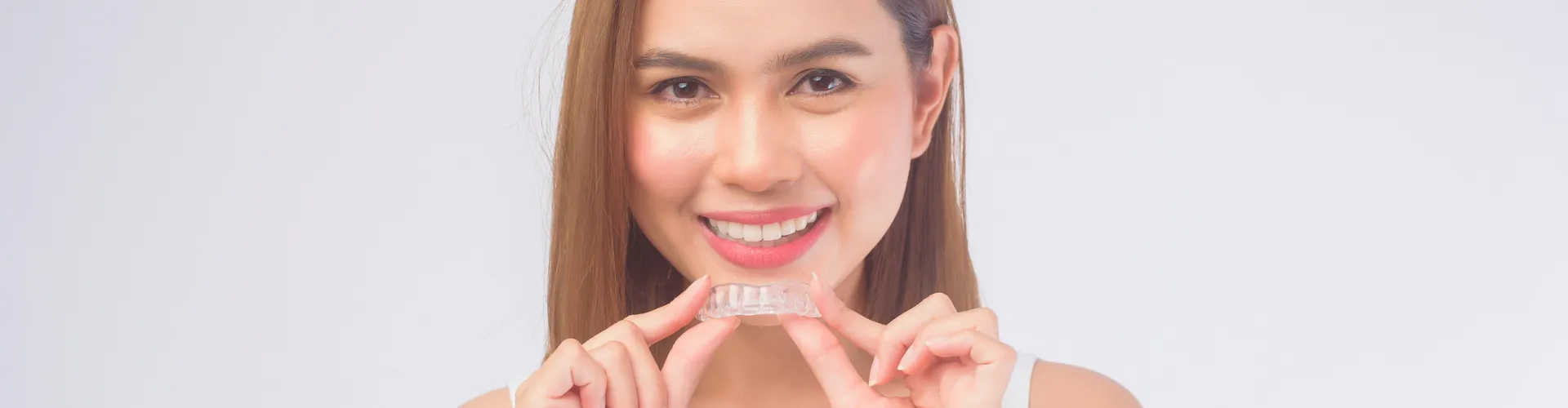 Smiling woman holding clear aligner in front of her mouth.