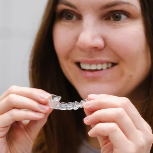 Smiling woman holding clear aligner in front of her mouth.